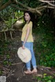 A woman standing under a tree holding a straw hat.