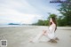 A woman in a white dress sitting on a beach.