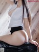 A woman in a white shirt and black shorts sitting on a black couch.