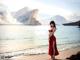 A woman in a red dress standing on a beach.