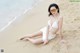 A woman in a white bikini sitting on the beach.