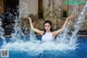 A woman in a white tank top is splashing water in a pool.