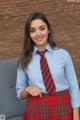 A woman in a blue shirt and red plaid skirt posing for a picture.