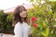 A woman in a white shirt holding a red flower.