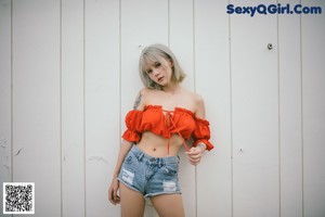 A woman in a red top and denim shorts posing for a picture.