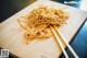 A wooden cutting board topped with noodles and chopsticks.